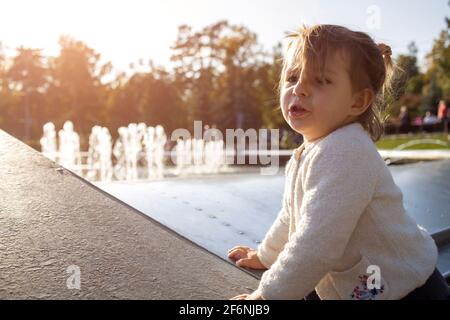 adorable petite fille fait des visages et des grimaces sur fond de parc. l'enfant joue avec gaieté. enfance heureuse Banque D'Images