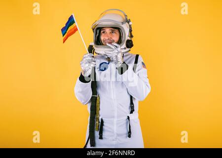 Cocosmonaute gay mâle en combinaison et casque, portant le drapeau arc-en-ciel lgtbi, sur fond jaune. Banque D'Images