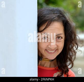 Charmante femme brune caucasienne mûre avec de longs poils peche autour d'un mur gris et fait une expression faciale heureuse devant un fond de parc. Banque D'Images