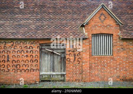 BUCKINGHAM, Royaume-Uni - 05 avril 2015. Ancienne ferme en briques ou bâtiment extérieur avec porte de grange en bois décorée de fers à cheval, Royaume-Uni Banque D'Images