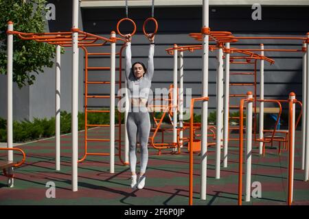 Jeune femme avec beau corps et ventre plat pend sur des anneaux de gymnastique. Sports de plein air. Banque D'Images