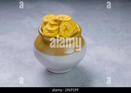 Croustilles de banane séchées ou gaufres de banane, magnifiquement arrangé dans une casserole d'argile et de céramique avec fond blanc texturé. Banque D'Images