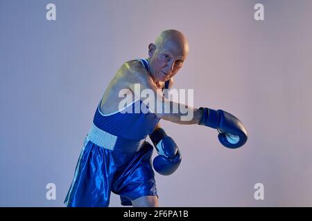 Homme senior portant des vêtements de sport de boxe isolés sur fond de studio gradient dans la lumière néon. Concept de sport, d'activité, de mouvement, de bien-être. CopySpace Banque D'Images