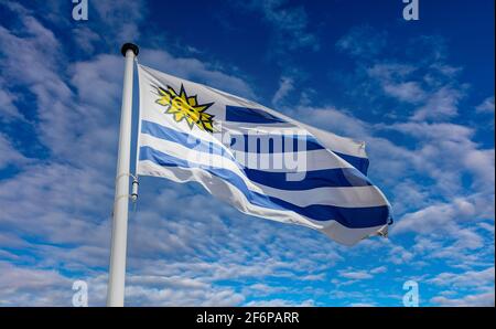 Drapeau de l'Uruguay, symbole national de la République orientale de l'Uruguay sur un mât agitant contre un ciel bleu nuageux Banque D'Images