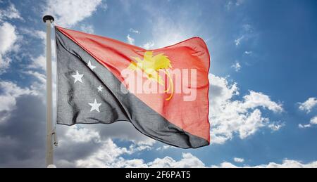 Drapeau de la Papouasie-Nouvelle-Guinée, symbole national de la PNG sur un mât agitant contre un ciel bleu nuageux Banque D'Images