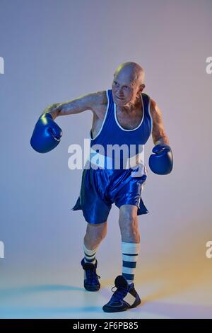 Homme senior portant des vêtements de sport de boxe isolés sur fond de studio gradient dans la lumière néon. Concept de sport, d'activité, de mouvement, de bien-être. CopySpace Banque D'Images