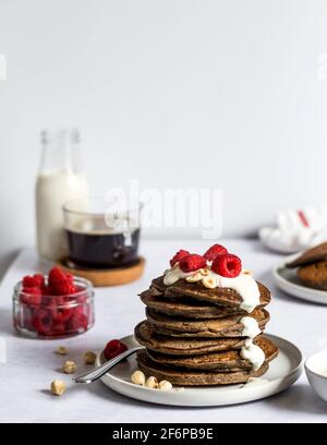 Petit-déjeuner le matin - table de cuisine avec une assiette de crêpes au tofu fraîchement préparées avec yaourt à base de plantes et framboises fraîches. Banque D'Images