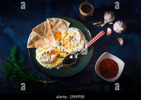 Plat d'œufs turc Cilbir, yogourt nature, œufs pochés, Ail, piment, de l'aneth frais et de beurre fondu. Orné de quelques morceaux de pain lavash un Banque D'Images