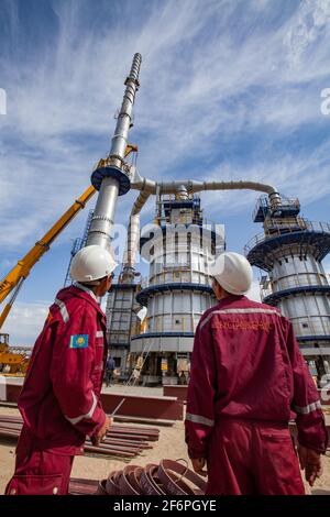 Aktau, Kazakhstan - 19 mai 2012 : construction de la colonne de la raffinerie de bitume asphaltique. Tour de distillation métallique, deux ouvriers et hydraulique jaune Banque D'Images