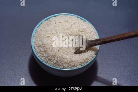 Riz cru servi dans une poêle à frire en porcelaine et une cuillère en bois sur fond sombre. Produit alimentaire humain. Nourriture naturelle. Grains de céréales éparpillés. Banque D'Images