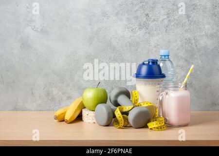 Cocktail de protéines, haltères, mètre ruban, bouteille d'eau et fruits frais sur table en bois Banque D'Images
