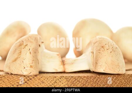 Deux moitiés de champignons frais bio appétissants sur un plateau rond en bambou avec un couteau en métal mis au point, gros plan, sur fond blanc. Banque D'Images