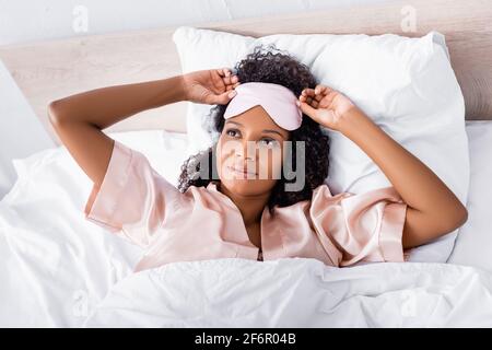 Vue de dessus de la femme afro-américaine dans le masque de sommeil et pyjama allongé sur le lit Banque D'Images