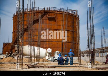 Aktau, Kazakhstan - 19 mai 2012 Construction d'une usine moderne de bitume asphaltique. Groupe de travailleurs, camion mélangeur de béton et réservoir de stockage d'huile Rusty. Activé Banque D'Images