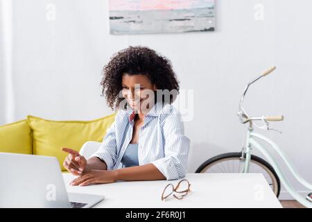 Un travailleur indépendant afro-américain positif pointant vers un ordinateur portable près de lunettes tableau Banque D'Images