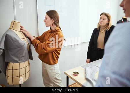 Femme en chemisier mettant des épingles dans le tissu sur le support de robe Banque D'Images