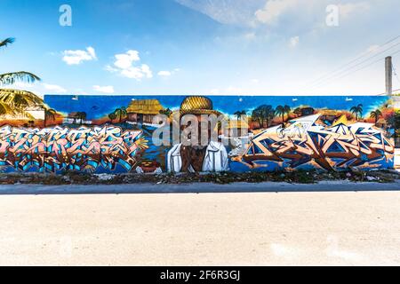 Art de rue dans une petite ville sur un long mur avec un vieil homme portant un chapeau de paille, une hutte rustique et des mots, avec un ciel bleu au-dessus du mur Banque D'Images