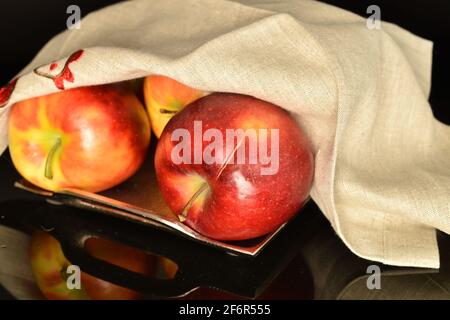 Plusieurs pommes rouges douces biologiques mûres Jonathan, gros plan, sur un plateau métallique, recouvert d'une serviette en lin. L'arrière-plan est noir. Banque D'Images