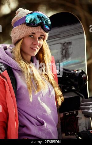 Femme snowboarder en costume brillant dans des lunettes de sport tient un snowboard. Sports extrêmes. Loisirs Banque D'Images