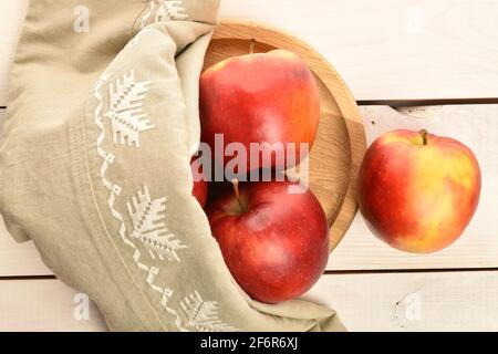 Un peu biologique, frais, mûr, juteux, savoureux, Pommes Red Jonathan, gros plan, sur un plateau rond en bambou, recouvert d'une serviette en lin, sur une wor en bois blanc Banque D'Images