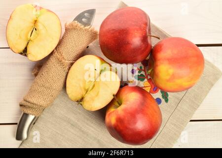 Trois pommes entières et deux moitiés, mûres fraîches, biologiques, rouges sucrées Jonathan, gros plan, sur une serviette en lin avec un couteau en métal enveloppé dans une serviette en jute, o Banque D'Images