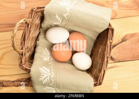 Deux œufs de poulet biologiques frais beige et deux blancs sur une serviette en lin, dans un panier tissé à partir de vignes, sur une table en bois naturel. Banque D'Images