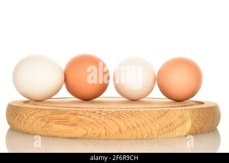 Quatre œufs de poulet frais bio délicieux, blancs et beiges, sur un plateau rond en bambou, sur fond blanc. Banque D'Images