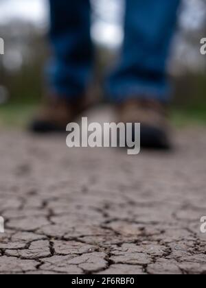 Terre aride photographiée après une sécheresse. Un homme marche le long d'un sentier de boue craqué au Royaume-Uni. Seules les chaussures et les pantalons sont visibles. Banque D'Images