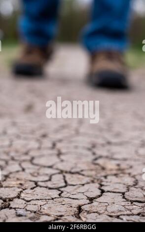 Terre aride photographiée après une sécheresse. Un homme marche le long d'un sentier de boue craqué au Royaume-Uni. Seules les chaussures et les pantalons sont visibles. Banque D'Images