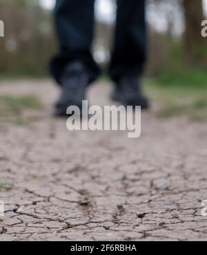 Terre aride photographiée après une sécheresse. Un homme marche le long d'un sentier de boue craqué au Royaume-Uni. Seules les chaussures et les pantalons sont visibles. Banque D'Images