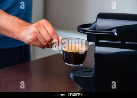 Gros plan de la main ramassant une tasse d'espresso de machine à café capsule à la maison. Concept de pause café. Banque D'Images