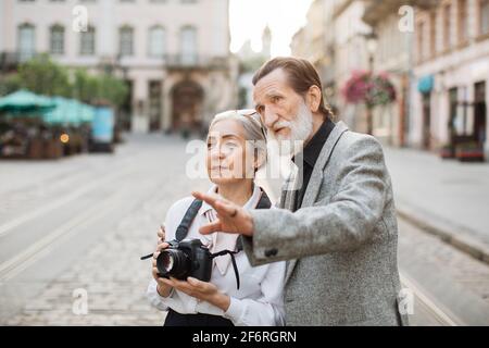 Belle femme mûre avec photo rétro sur le cou écoutant son mari barbu qui l'embrasse. Famille senior appréciant le temps de voyage pendant la retraite. Passer du temps ensemble. Banque D'Images