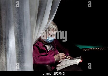 Vieille femme assise par la fenêtre de sa résidence faisant un puzzle de recherche de mot, Barcelone, Espagne Banque D'Images