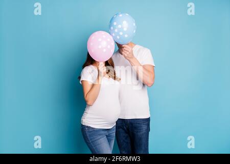 Photo de couple enceinte couvrir le visage avec des ballons porter blanc tee-shirts isolés sur fond bleu sarcelle Banque D'Images