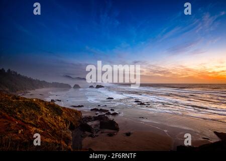 Vue sur une plage de Cannon brumeux depuis le parc national d'Ecola, dans l'Oregon, au coucher du soleil. Banque D'Images