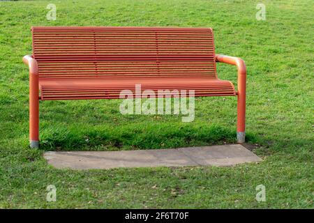 Banc de métal orange dans le parc entouré d'herbe verte lumineuse, belle journée dans le parc communautaire, banc de métal vide unique Banque D'Images