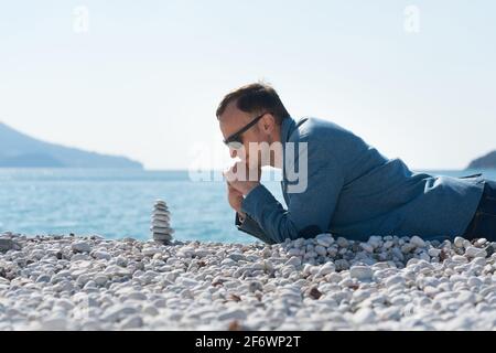 un homme dans une veste se trouve sur la plage et regarde la pyramide zen Banque D'Images