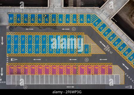 Parking vu directement du dessus, avec des rangées de véhicules et des places de stationnement marquées créant des motifs et des lignes géométriques forts. Banque D'Images