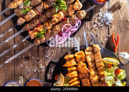 Émincé de kebab sur une brochette de métal avec sauce, tranches de concombres, tomates et oignons sur un plateau en bois Banque D'Images