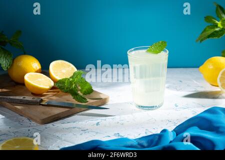 Verre avec limonade et citrons sur table en bois, boisson rafraîchissante froide avec glace sur fond clair. Banque D'Images