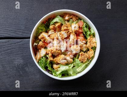 salade césar fraîche avec viande de poulet frite dans un récipient en papier à emporter sur une table en bois noir, vue du dessus Banque D'Images