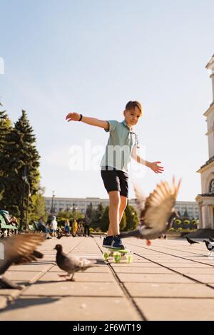 Un garçon de la planche de penny dans le parc sur un l'été est chaud avec des pigeons et du ciel Banque D'Images