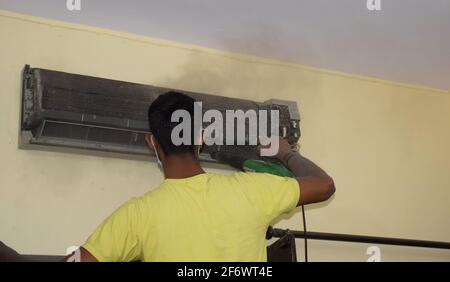 Un mécanicien de la climatisation indienne retire la poussière du climatiseur fendu à l'aide d'une soufflerie d'air Banque D'Images