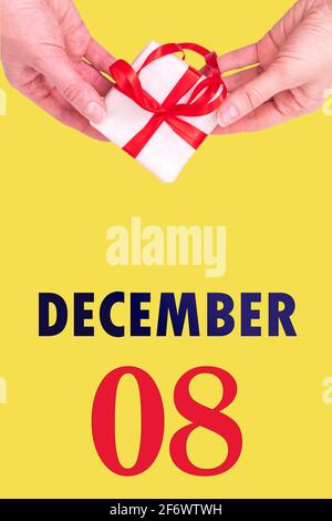 8 décembre. Calendrier vertical de fête avec mains tenant boîte cadeau blanche avec ruban rouge et calendrier Date 8 décembre sur fond jaune illuminant Banque D'Images