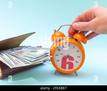 Concept de gestion du temps. Une main tient un réveil orange et des dollars dans un portefeuille ouvert sur fond bleu, espace de copie. Concept de réussite commerciale Banque D'Images