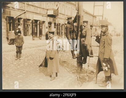 La photo montre un groupe de soldats qui ont mis en place pour le photographe pour montrer comment installer les câbles téléphoniques. Le groupe a été organisé de manière à afficher clairement tous les éléments nécessaires à la tâche. L'homme à gauche porte une position avec un tambour de câble sur son dos. Son collègue du côté droit tient des crochets en fer avec des isolateurs dans la main et une échelle. Les deux soldats du milieu ont grimpé un peu sur un nouveau poste téléphonique à l'aide d'un fer à repasser. On a une posture très détendue et regarde directement à la caméra .. La photo montre un groupe de soldats qui se sont mis en place pour le photographe Banque D'Images