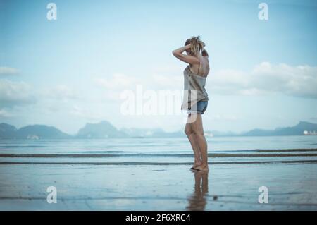 Vue latérale d'une femme debout sur la plage mettant ses cheveux dans une queue de poney, Koh Yao, Phang Nga, Thaïlande Banque D'Images