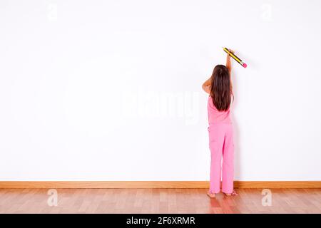 Petite fille avec un crayon géant écrivant sur le mur Banque D'Images