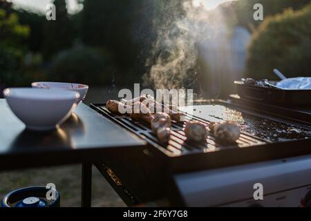 Gros plan d'un barbecue grill avec des viandes cuisant sur eux, le soleil brille dans le fond est attrapant la fumée Banque D'Images