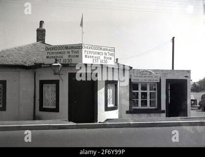 1957, vue historique et extérieure de la célèbre Horse Shoe Marriage Room, à Gretna Green aux frontières écossaises, établie comme le signe sur le bâtiment d'un étage dit en 1830 et à cette époque, avec plus de 10 000 mariages exécutés là. À cette époque, l'entrée de la salle de mariage était par 'Ye Old Toll Bar', la première maison d'Écosse et où des souvenirs et des cartes postales étaient disponibles à l'achat. Le Old Toll Bar, Gretna, est devenu une partie de l'héritage de mariage à l'écart en 1830, quand un pont a été construit au-dessus de la rivière Sark, redirigeant la majeure partie de la circulation vers l'Écosse. Banque D'Images